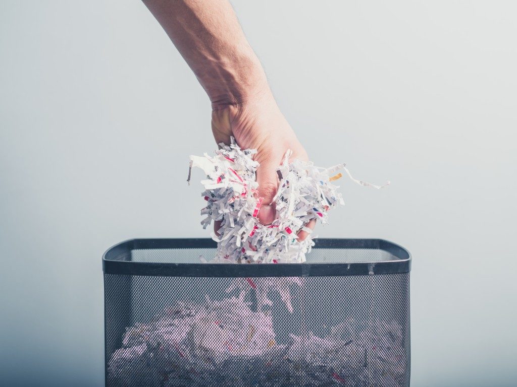 person putting shredded papers in the trash can
