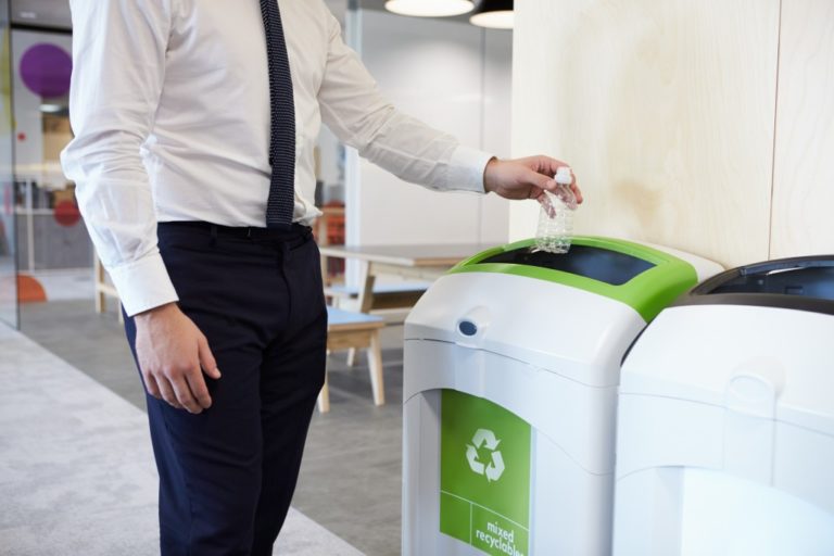 man throwing his empty bottle on a recycling bin