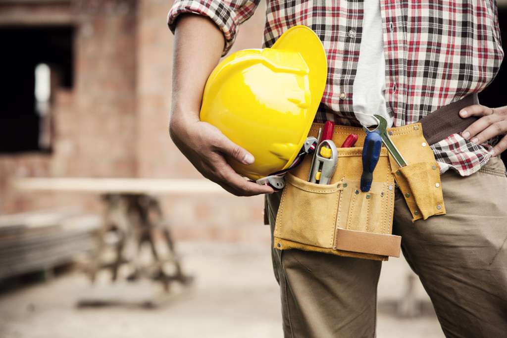A construction worker holding a yellow hard hat while wearing a a tool belt