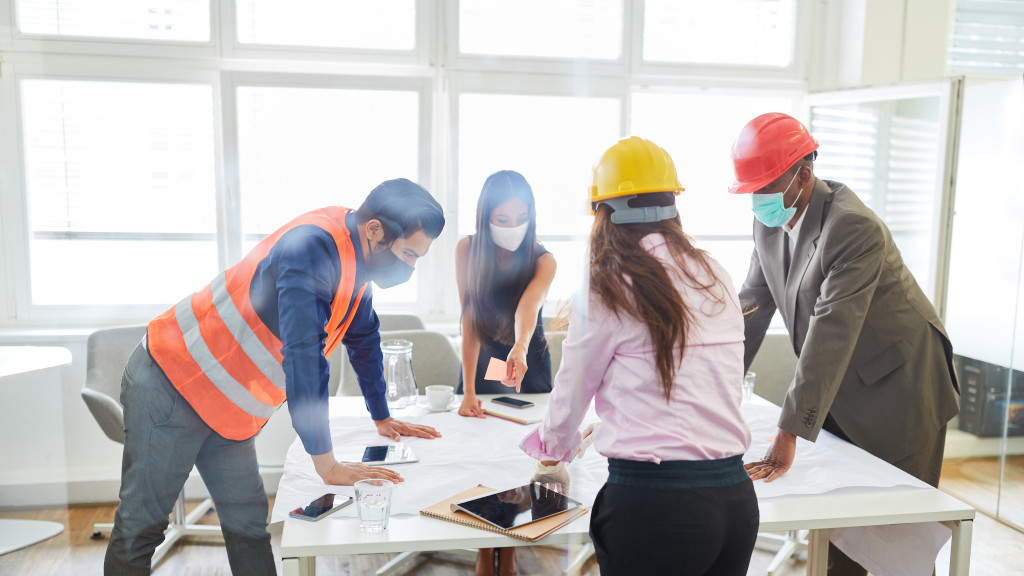 Group of builders with face masks and hard hats discussing blueprints