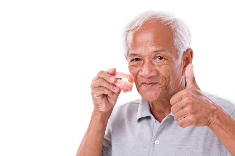 An old man holding his dentures while giving a thumbs-up to the camera