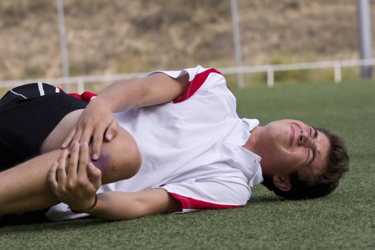A footballer holding his bruises knee while laying on the field