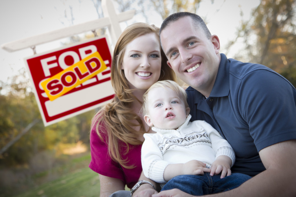 A family smiling with sold property signage behind