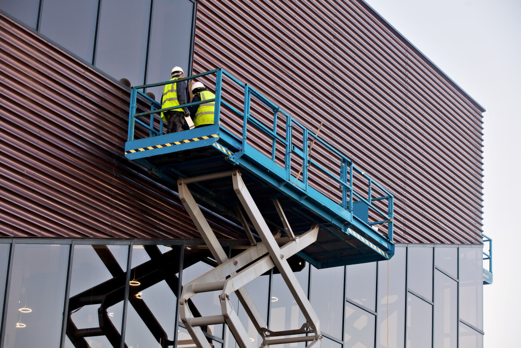 two male builders on top of a scissor lift platform at the side of the building